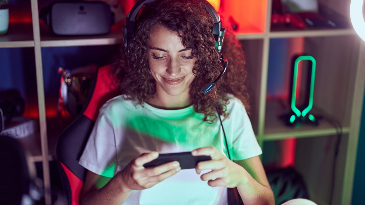 A young hispanic woman streamer using a smartphone and gaming computer in her studio