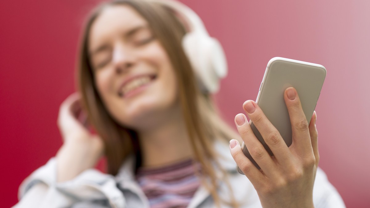 Close-up of headphones draped over a smartphone tapping the heart save icon on a music track
