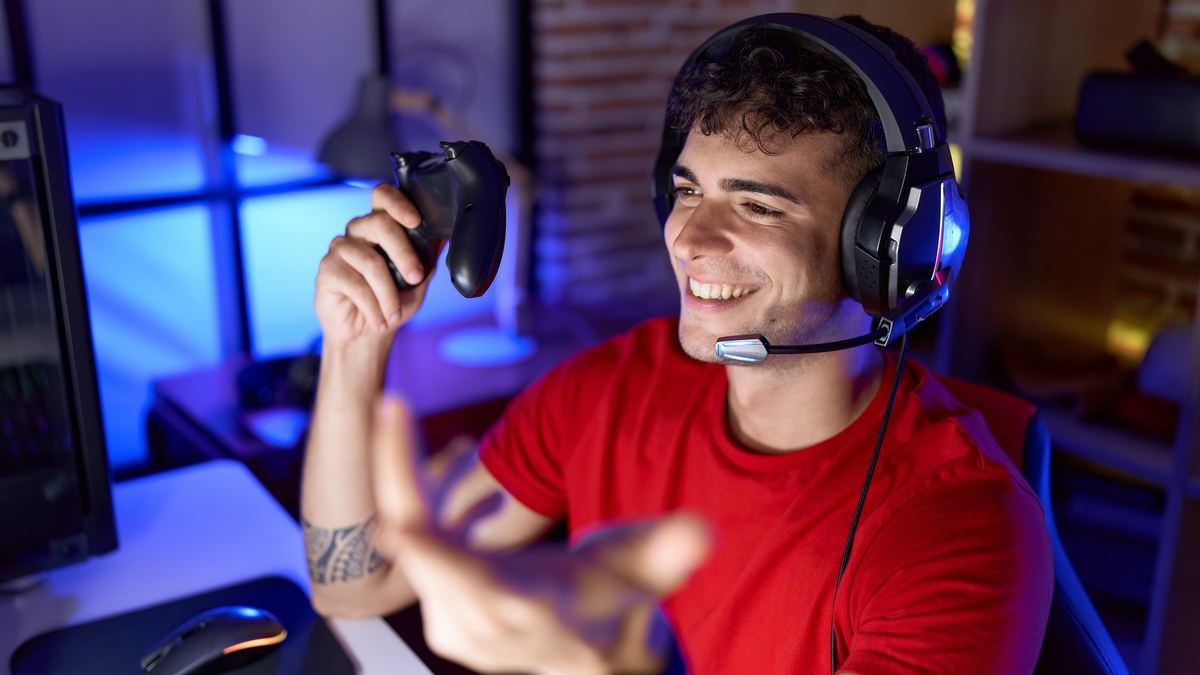 Young gamer wearing headset sitting in gaming room with illuminated monitors chatting on Discord