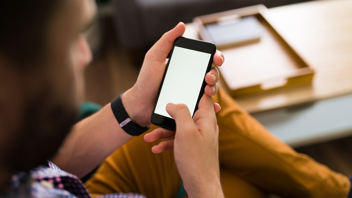 A person holding a modern iPhone device interacting with a native mobile application interface