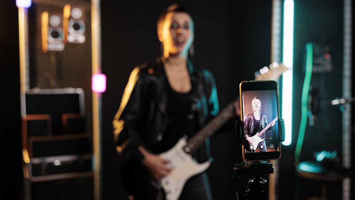A female guitarist recording performance video with smartphone on tripod in music studio