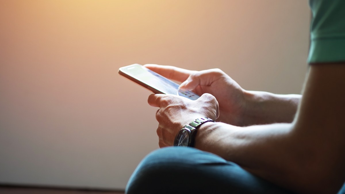 A person holding a modern smartphone scrolling through a social media profile link on touchscreen