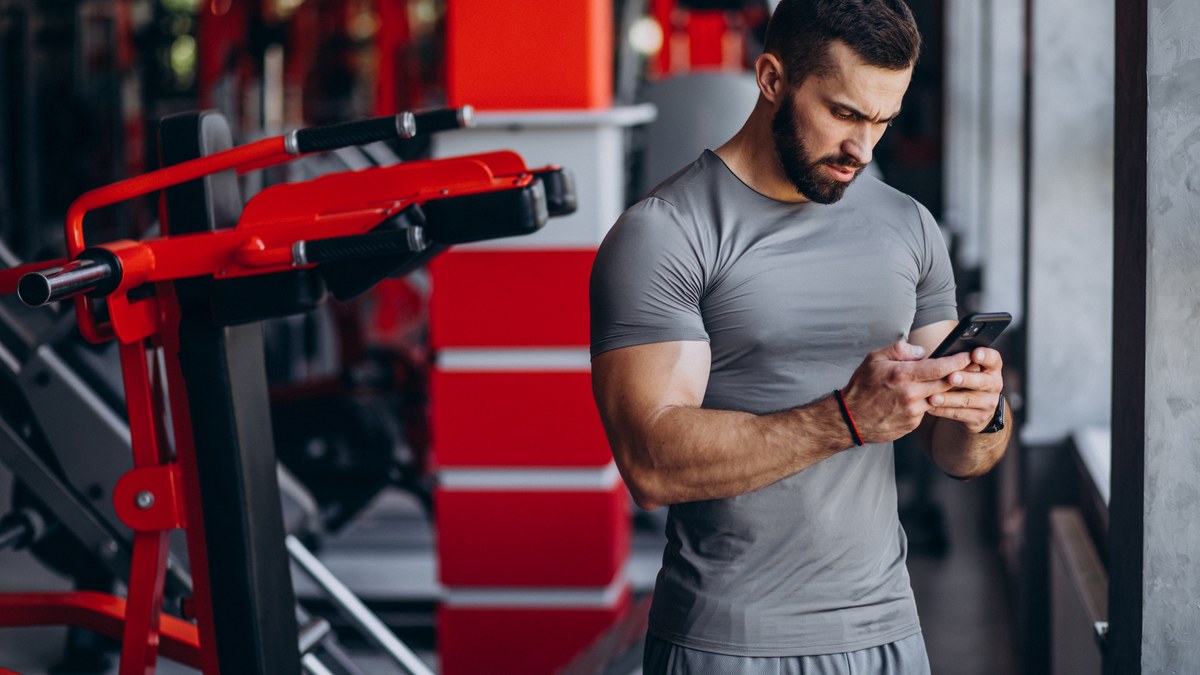 Personal trainer holding a smartphone in a gym demonstrating workout tracking and coaching applications