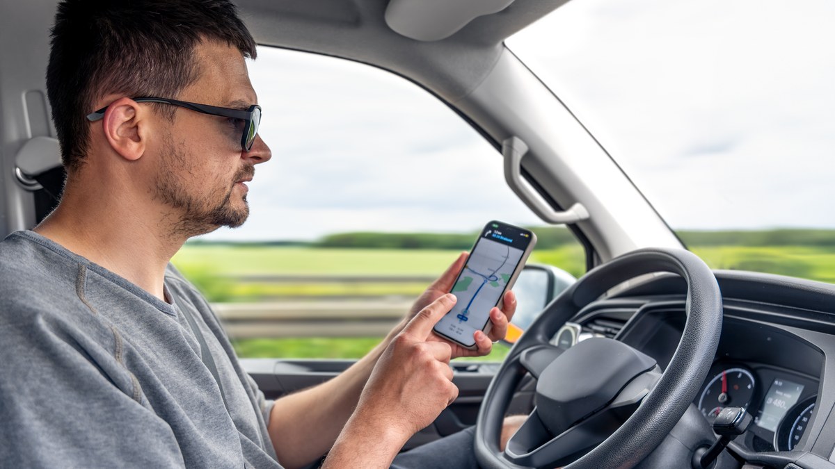 A driver holding a smartphone with GPS navigation mounted on a car dashboard