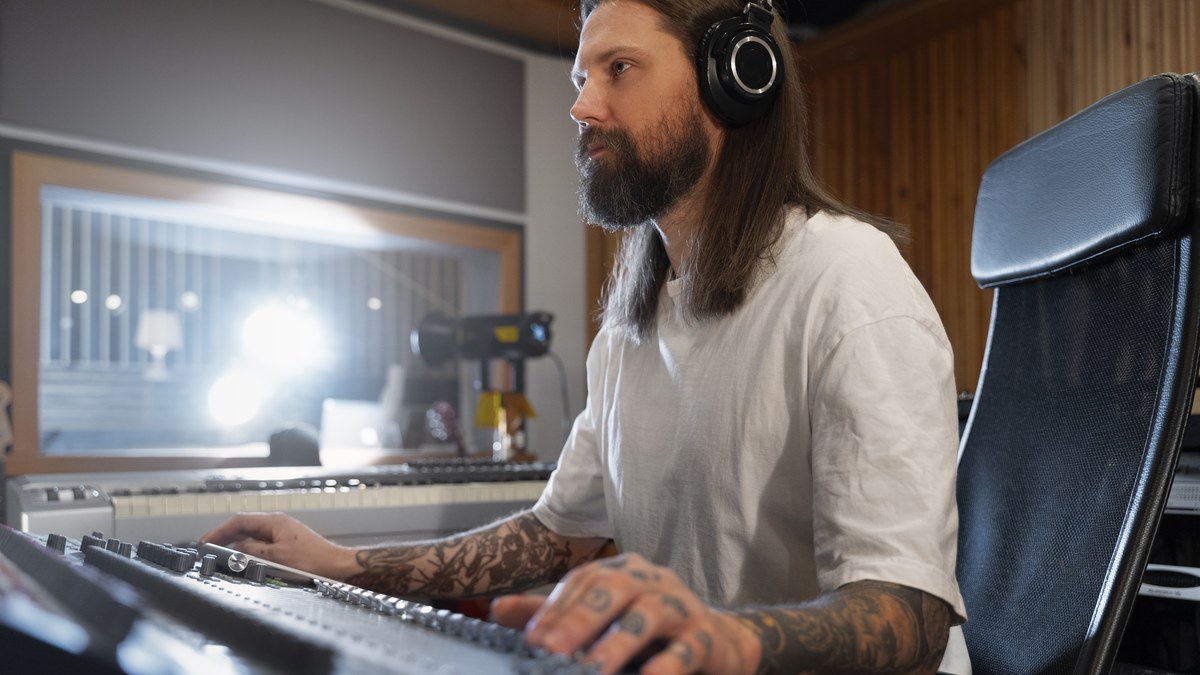 A music producer and sound engineer working on a professional audio mixing console with studio headphones