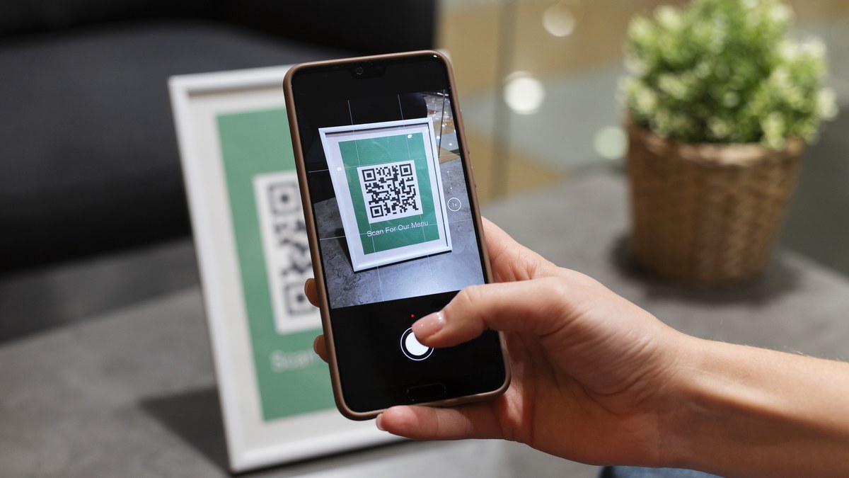 Close-up of a person holding a smartphone camera pointed at a modern QR code graphic
