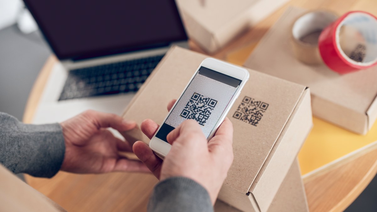 A retail warehouse team member scanning a high-contrast QR code on product packaging using a smartphone camera