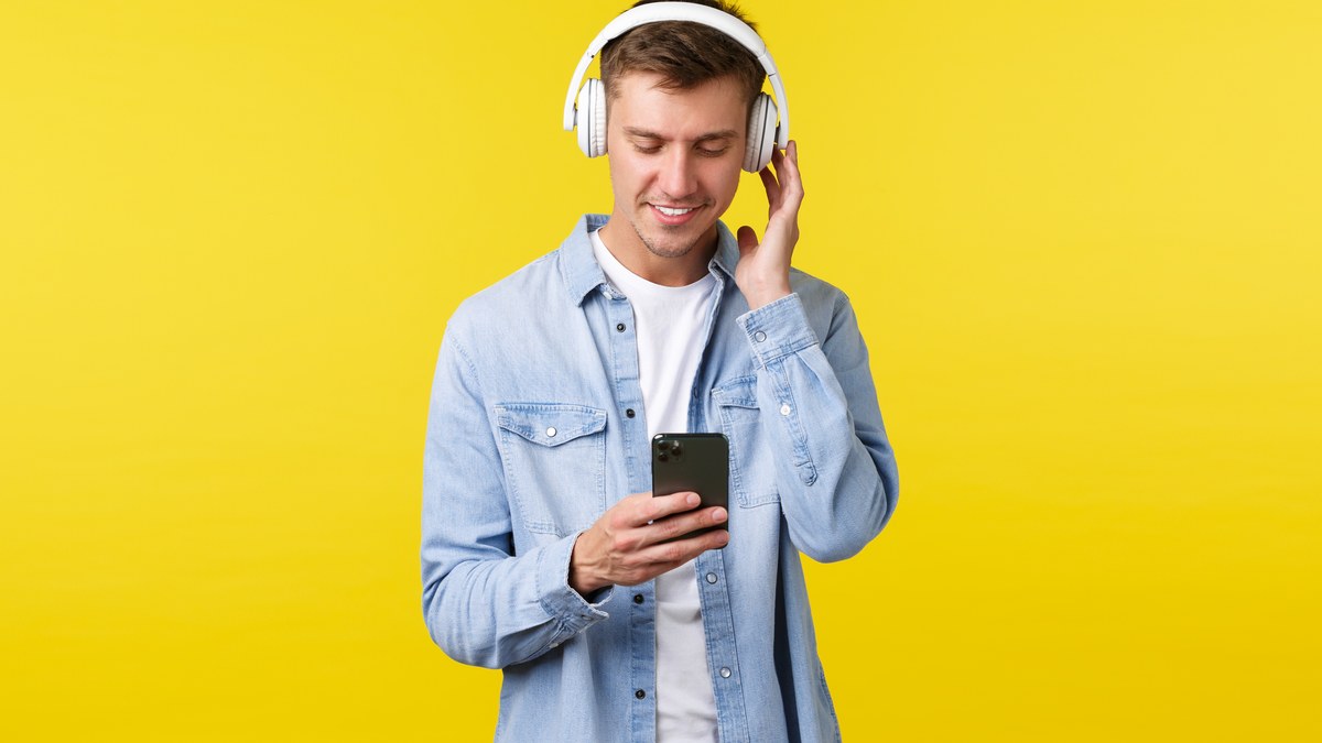 Young man wearing headphones and using smartphone to stream Spotify playlist