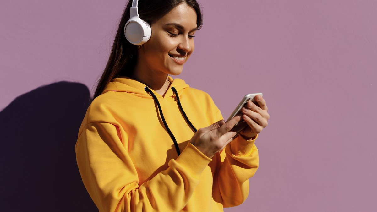 Person wearing headphones while listening to a music streaming playlist on a mobile phone