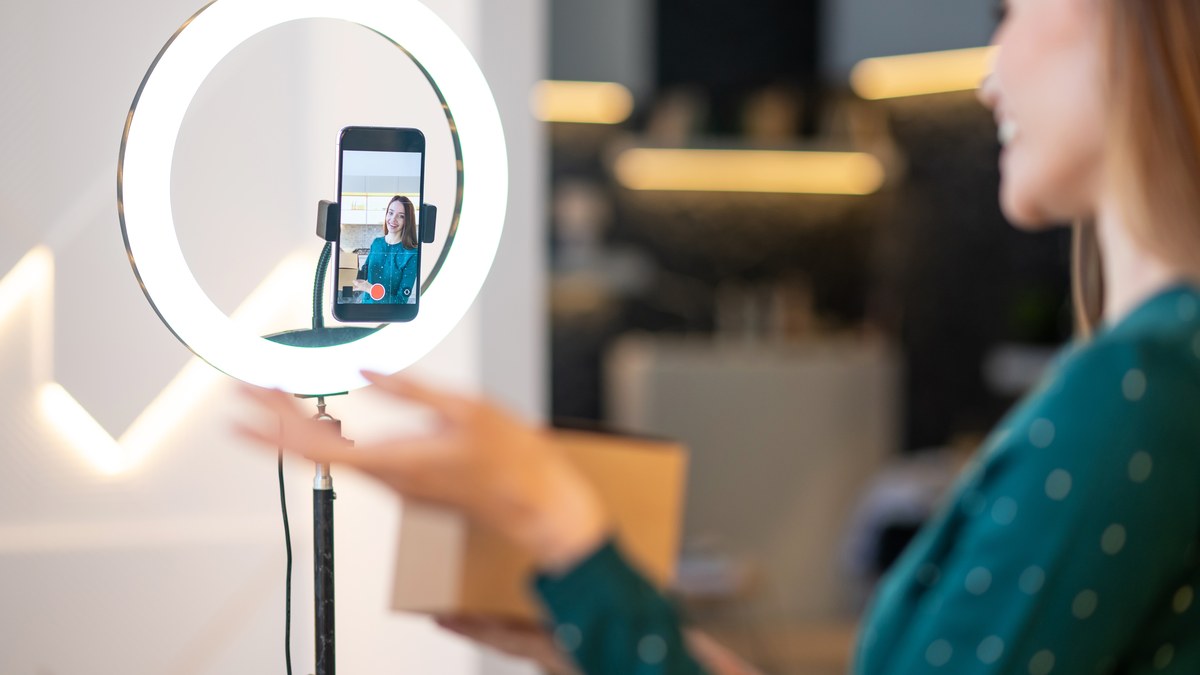 Creator recording sponsored TikTok video with smartphone on ring light tripod showcasing mobile app