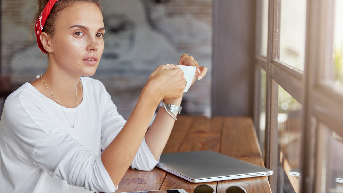 Freelance creator working on a laptop at a coffee shop desk with a digital tip jar link
