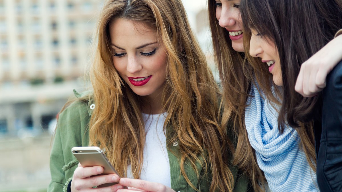 Group of friends on a city street smiling and looking at a shared mobile messaging app